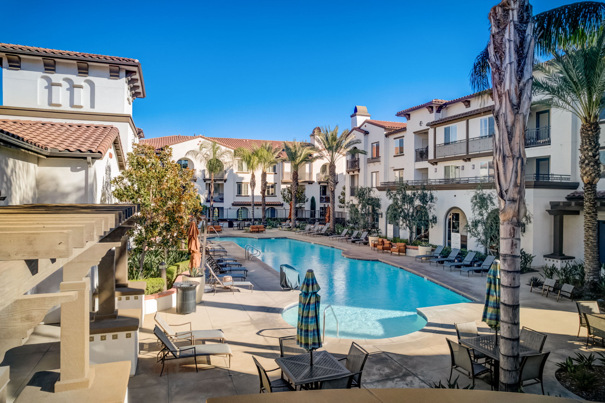 Spacious pool area at Vistara Apartments with tables, umbrellas, and BBQ stations, offering a relaxing and social space for residents